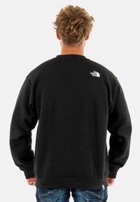 Sudadera negra de algodón, con cuello redondo y mangas largas. Logo blanco notable en la parte posterior, cerca del cuello.