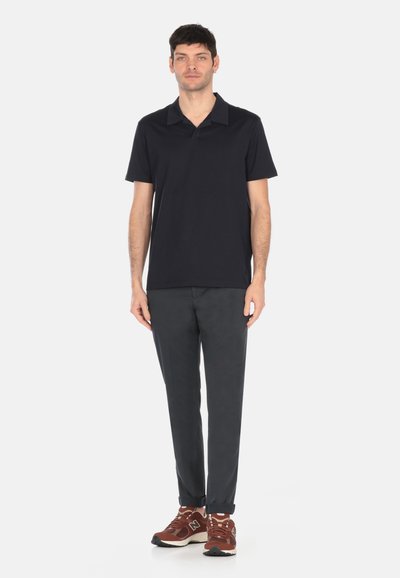 Camisa polo azul marino con cuello plano, combinada con pantalones oscuros grises. Zapatillas marrones con suela en contraste y detalles estampados.