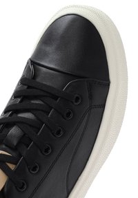 Sneaker nera in pelle con suola in gomma bianca texturizzata, caratterizzata da lacci neri e un punta liscia, evidenziata da un accento laterale beige.