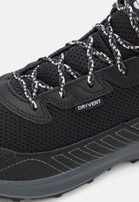 Chaussure de randonnée noire avec tissu en maille, superpositions synthétiques texturées, lacets noir et blanc, et un label "DRYVENT". Semelle en caoutchouc avec motif.