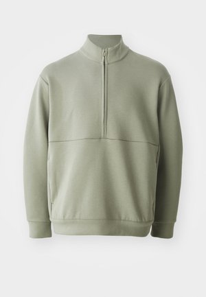 Suéter de manga larga verde claro con un cuello alto y media cremallera. Textura suave con un detalle de costura horizontal en el pecho.