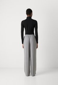 Svart langermet turtleneck-genser kombinert med løse, lysegrå bukser med elastisk midje og subtil diagonaal tekstur.
