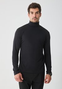 Czarny sweter z golfem z miękkiego materiału, z długimi rękawami i dopasowanym krojem. Noszony z czarnymi spodniami, prezentowany na neutralnym tle.