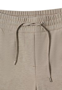 Pantalons de jogging beiges avec une taille élastique, une fermeture par cordon de serrage et un petit accent argenté sur la poche latérale. Texture lisse et coupe ajustée.