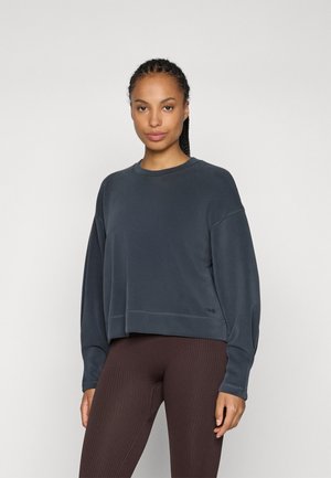 Temno modra skrajšana sweatshirts, lahka tkanina, okrogla ovratnica, spuščeni ramenski šivi, kontrastno šivanje, subtilna podrobnost logotipa na robu.