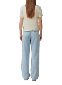 Jasno beżowa bluzka z krótkim rękawem w połączeniu z oversize'owymi jasnoniebieskimi dżinsami, ukazującymi luźny krój i lekko skrócony fason.