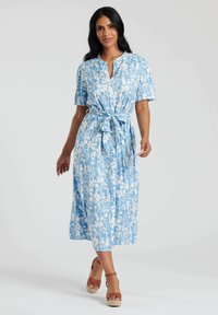 Niebieska sukienka w kwiatowy wzór z krótkimi rękawami, z buttonem przy dekolcie oraz paskiem w talii. Materiał wydaje się lekki i zwiewny.