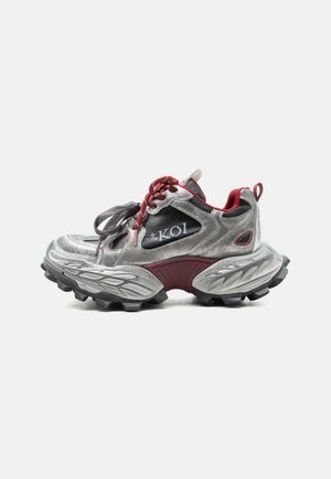 Strieborná a bordová teniska s hrubou textúrovanou podrážkou, červenými šnúrkami, čiernymi sieťovinovými panelmi a označením "KOI" na boku.