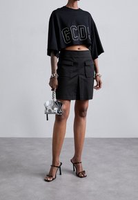 Camiseta negra corta con letras blancas, combinada con una falda mini negra con bolsillos. Los accesorios incluyen una cadena de plata y un bolso pequeño.
