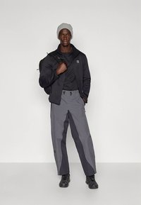 Herreutendørsantrekk med svart fleecejakke, svart t-skjorte, grå vanntette bukser med sidedetaljer og svarte joggesko. Grå lue inkludert.