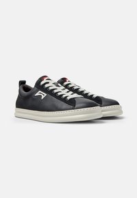 Pair of black leather sneakers with white laces, white soles, and a white logo on the side, shown on a plain gray background.