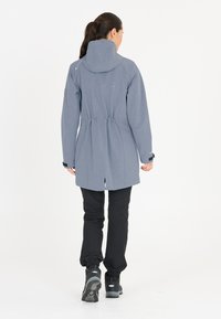 Water-resistant gray jacket with a cinched waist, high collar, and zippered pockets, paired with black pants and sturdy hiking boots.
