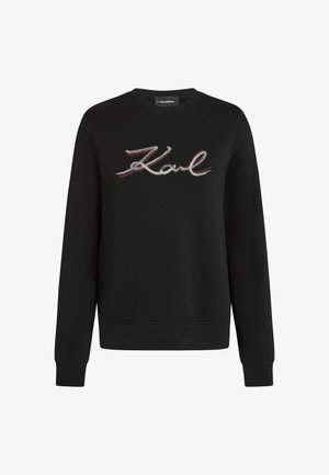 Crna dukserica dugih rukava s okruglim izrezom, na kojoj se preko grudnog dijela nalazi riječ "Karl" izvedena u šljokičastom kurzivnom pismu.