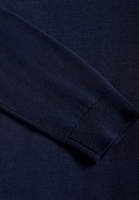Manche de pull en maille bleu marine avec détail de bord-côte, montrant une texture fine de maille et des coutures.
