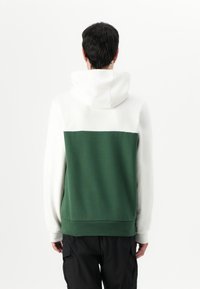 Felpa con cappuccio caratterizzata da una sezione superiore bianca e una inferiore verde, realizzata in tessuto morbido con polsini e orlo a coste.