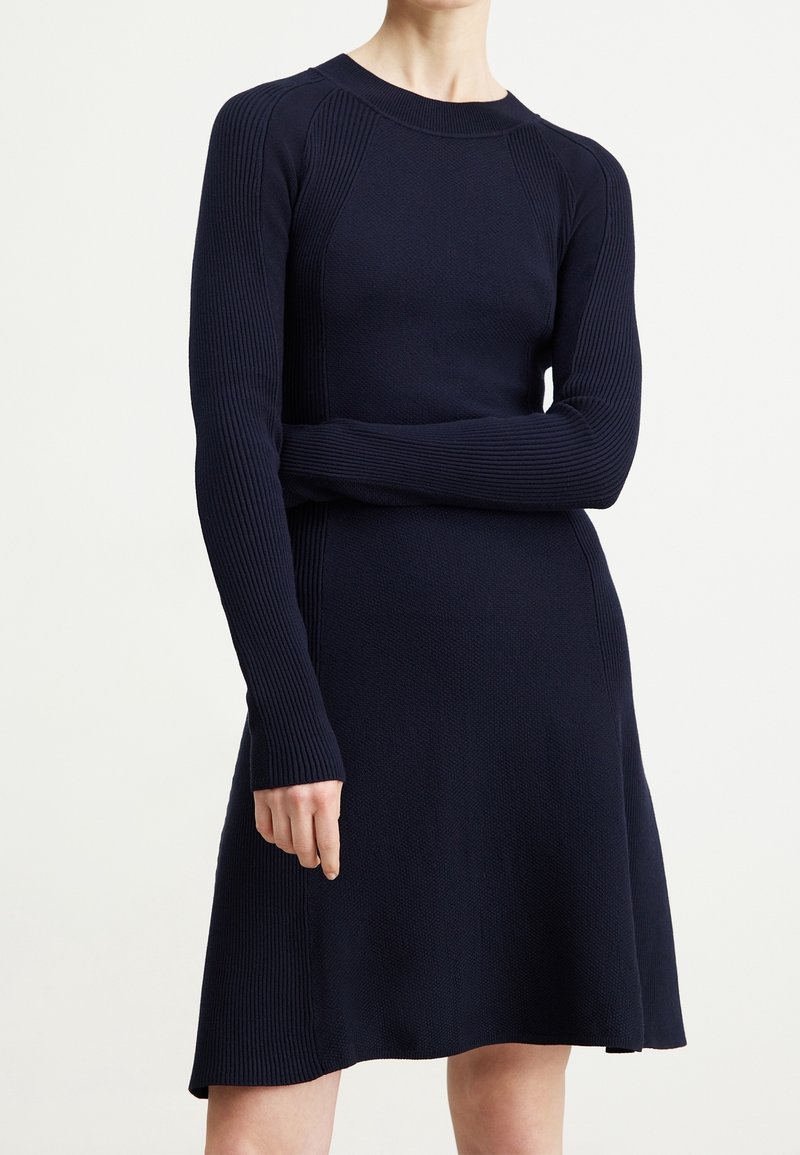 Granatowa sukienka z dzianiny prążkowanej, z długimi rękawami, dopasowanym górnym partem i rozkloszowanym dołem, ze zdobieniem teksturowanym wzdłuż szwów.