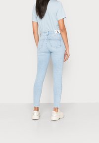 Jeans de tiro alto en azul claro con un ajuste elástico, que incluyen bolsillos traseros y una cinturilla con marca, combinados con calzado blanco.