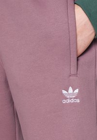 Ljuslila sweatpants i mjukt tyg, med sidfickor och en vit broderad logotyp. Midjebandet är elastiskt.