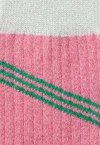 Șosete sportive tricotate cu un design roz cu dungi, având o bandă albă deasupra și două dungi verzi care accentuează secțiunea roz.