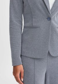 Grå texturerad blazer med en enkel knappstängning, skräddarsydd passform och elegant design. Har två sidofickor och en slät tygfinish.
