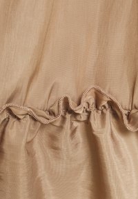 Un tessuto marrone chiaro con una trama liscia presenta un ruffle arricciato lungo il bordo, che mette in risalto una leggera lucentezza e dettagli di cucitura delicati.