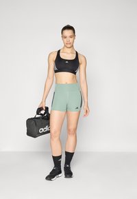 Must värvi sportlik rinnahoidja kolme valge triibuga, rohelised kõrge vöökohtadega lühikesed püksid külgtriipudega, mustad sokid ja must Adidas'i spordikott.