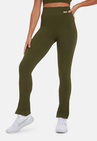 Olijfgroene geribbelde leggings met een hoge tailleband, voorzien van een kleine zilveren accent. Gemaakt van rekbaar materiaal, uitlopend bij de enkels.