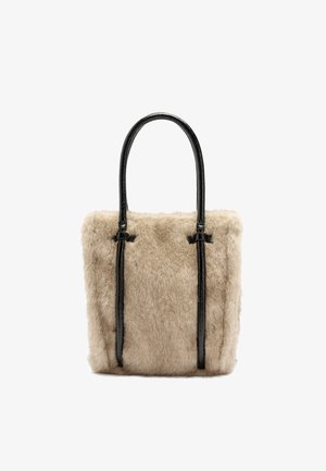 Beżowa torba typu tote z futerkiem z materiału syntetycznego, z połyskującymi czarnymi skórzanymi uchwytami, w kształcie prostokąta i z przeszyciami na górze. Miękka tekstura.