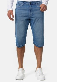 Shorts de mezclilla en azul claro con diseño de cinco bolsillos, dobladillo cosido y corte ajustado. Combinados con zapatillas blancas.