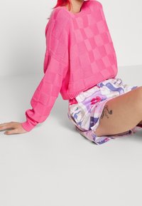 Rosa stickad tröja med en strukturerad rutmönster. Kombinerad med mönstrade shorts i pastellfärger som har blommönster.