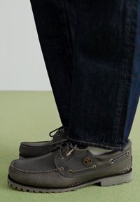 Szare skórzane buty żeglarskie z sznurkami, okrągłym noskiem, widocznymi przeszyciami, gumową podeszwą i małym logo po boku, w połączeniu z ciemnymi dżinsami.