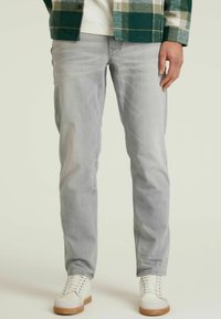 Vaqueros de un gris claro con un corte ajustado, que presentan un ligero desgaste. Combinados con zapatillas blancas y una camisa de cuadros verde.