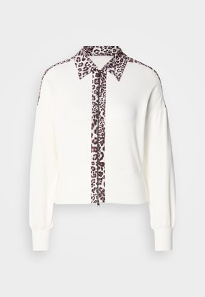 Cardigan blanc avec des accents imprimé léopard sur le col et le devant, doté d'une fermeture éclair et de poignets côtelés. Texture en maille douce.