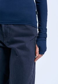 Navy Langarmoberteil mit Daumenlöchern, kombiniert mit dunkelblauen Hosen. Das Oberteil verfügt über einen glatten, dehnbaren Stoff und einen abgerundeten Saum.