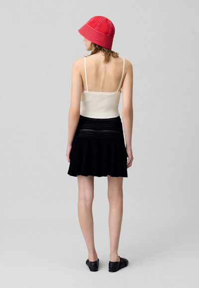Top in cotone bianco a righe, gonna mini plissettata nera, cappello a secchiello rosso. Tessuto liscio, gonna svasata, morbida al tatto, vista posteriore. Ballerine nere.