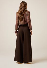 Bruine wijde broek met hoge taille, gecombineerd met een doorschijnende bloes met een bloemenprint in gedempte kleuren. Gladde textuur, casual pasvorm.