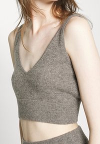 Top corto grigio a maglia con scollatura a V profonda e orlo a coste, caratterizzato da una texture morbida e un design senza maniche.