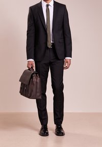 Svart slim-fit kostym med en vit skjorta och olivgrön slips, accentuerad av en brun läderportfölj och svarta formella skor. Rena snitt, skräddarsydd design.