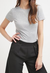 Camiseta de manga corta con rayas grises y blancas, cuello redondo, combinada con pantalones negros de talle alto. Textura de tela suave.