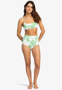 Biele bikiny s tropickým vzorom zelených listov; top s tenkými ramienkami, nohavičky s vysokým pásom; hladká textura, elastický materiál.