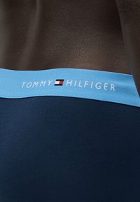 Λωρίδα μέσης σε ναυτικό εσώρουχο με ανοιχτό μπλε ταινία που δείχνει το λογότυπο Tommy Hilfiger και το όνομα της μάρκας σε σκούρο δέρμα.