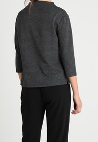 Top negro texturizado con mangas tres cuartos y cuello alto, combinado con pantalones negros; diseño simple y de corte recto.