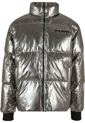 Ezüst színű púpos dzseki magas gallérral, cipzáras záródással és fekete márkázással. Fényes textúrával és elasztikus mandzsett ákkal rendelkezik a szoros illeszkedésért.