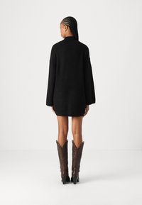 Black oversized knit sweater dress with long sleeves, textured fabric, and a high collar. Paired with dark brown knee-high cowboy boots.