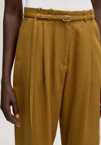 Khaki high-waisted broek van gestructureerde stof met een gestrikt riem en een metalen ringaccent. Beschikt over steekzakken en een losse pasvorm.