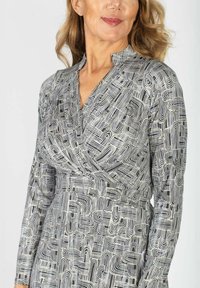 Pitkähihainen mekko, jossa on mustavalkoinen abstrakti kuvio, valmistettu sileästä kankaasta, V-pääntiellä ja kootulla vyötäröyksityiskohdalla.