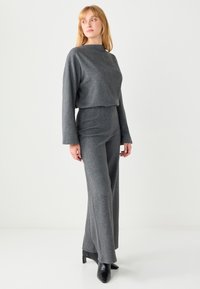 Maglione grigio corto con maniche lunghe e colletto piatto abbinato a pantaloni grigi a vita alta, caratterizzati da una texture morbida e un tessuto liscio.