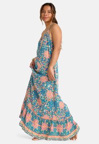 Bloemrijke maxi-jurk in teal met roze en oranje patronen, met spaghettibandjes en een geplooide zoom. Lichtgewicht stof met een vloeiende uitstraling.