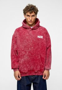 Rode tie-dye hoodie met een kangoeroezak, met een witte bedrukte logo "ESCAPE FROM THE POLIZIE" op de linkerborst.