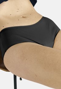 Musta bikinitruseri sileällä pinnalla ja joustavalla vyötäröllä, minimalistisella muotoilulla ja istuvalla rakenteella vaalealla ihon sävyllä.